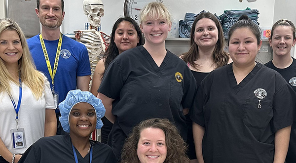 Madison, surrounded by coworkers in room with supplies including a life-size human skeleton model