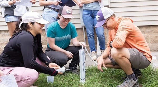 students crouched near testing equipment in lawn in front of a house